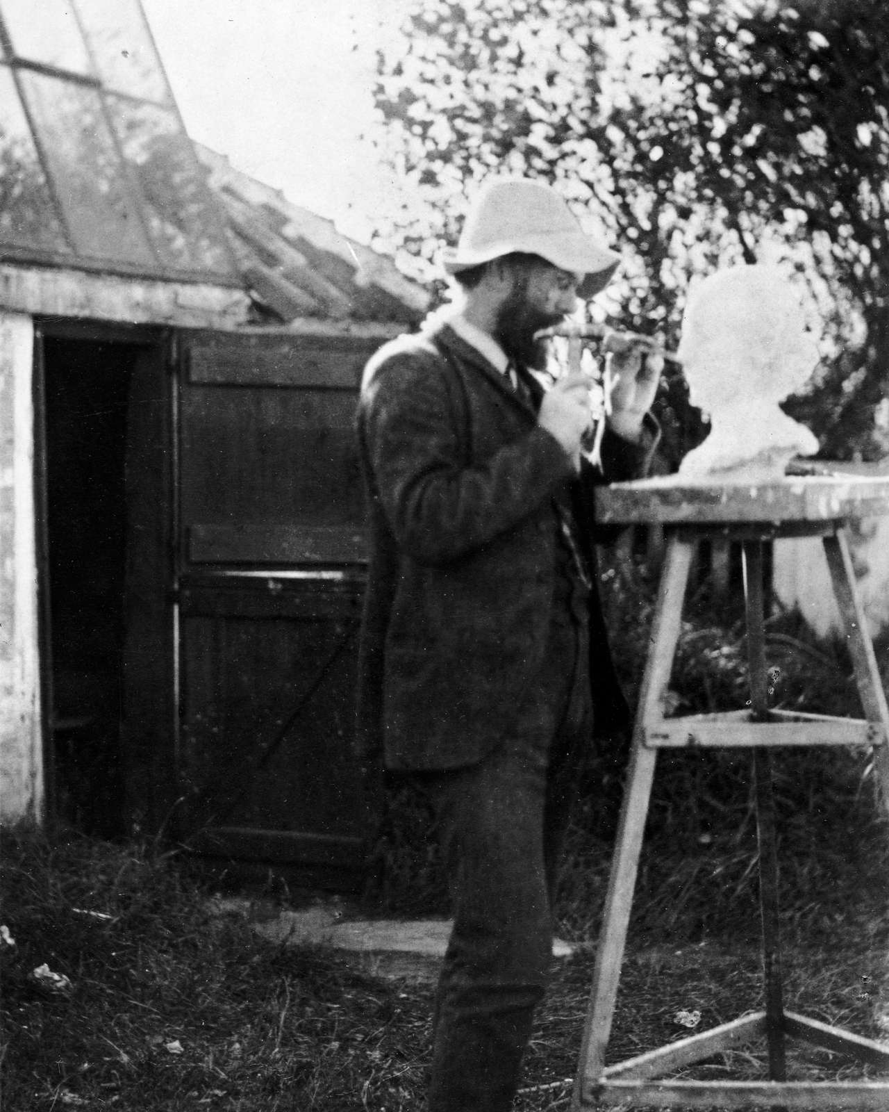 P.S. Krøyer arbejder på busten af Anna Ancher uden for atelieret i korntørringsmagasinet. Skagen. U.å. Skagens Kunstmuseers historiske fotosamling.