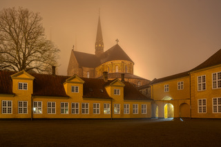 Roskilde Cathedral a foggy night, behind the courtyard of the yellow Royal Palace in Roskilde