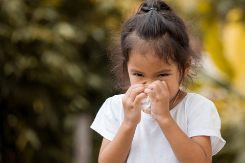 Sick little asian girl wiping or cleaning nose with tissue on her hand