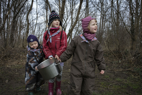 Tre piger bærer stor gryde i skoven til spilopspejd
