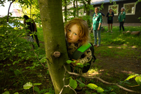 Pige gemmer sig bag træ i skoven til spilopspejd