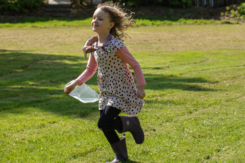 Pige løber med plastikpose på græsset til spilopspejd