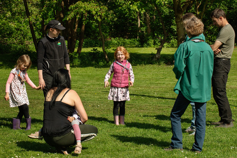 Pige og forældre i cirkel på græs til spilopspejd