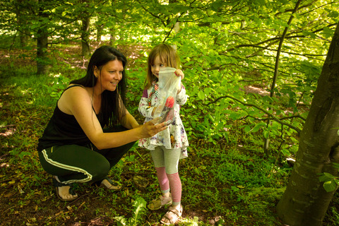 Voksen og pige holder syltetøj op i pose i skoven til spilopspejd