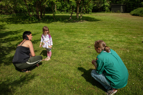 Voksen sidder på hug og taler til pige på græsplæne til spilopspejd