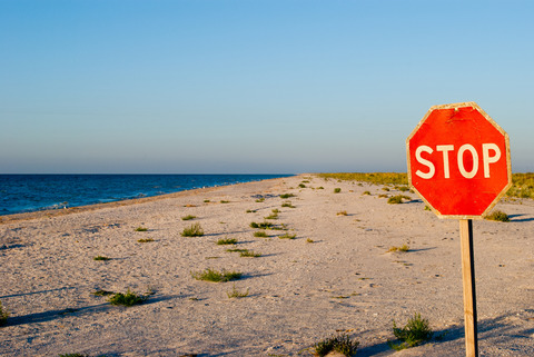 big red road prohibiting stop sign standing on a deserted beach yellow sand blue sea shore clear blue sky summer warmth