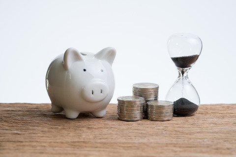 Finance or investment time with hourglass or sandglass, piggy bank and stack of coins on wooden table with white background